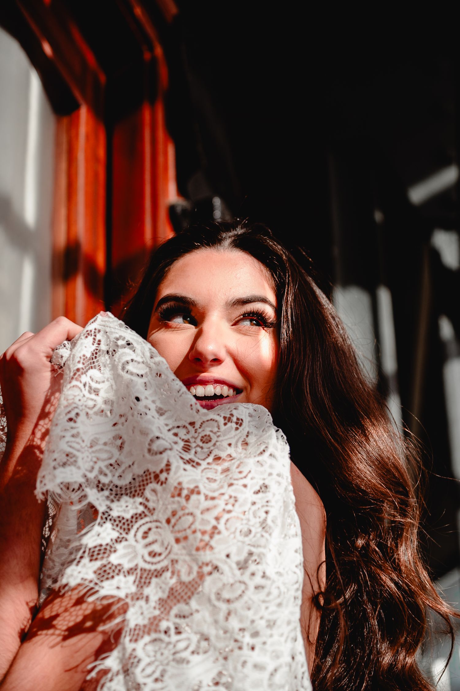 Close-up of someone in joyful laughter holding delicate white lace fabric against a dark background with orange accents.