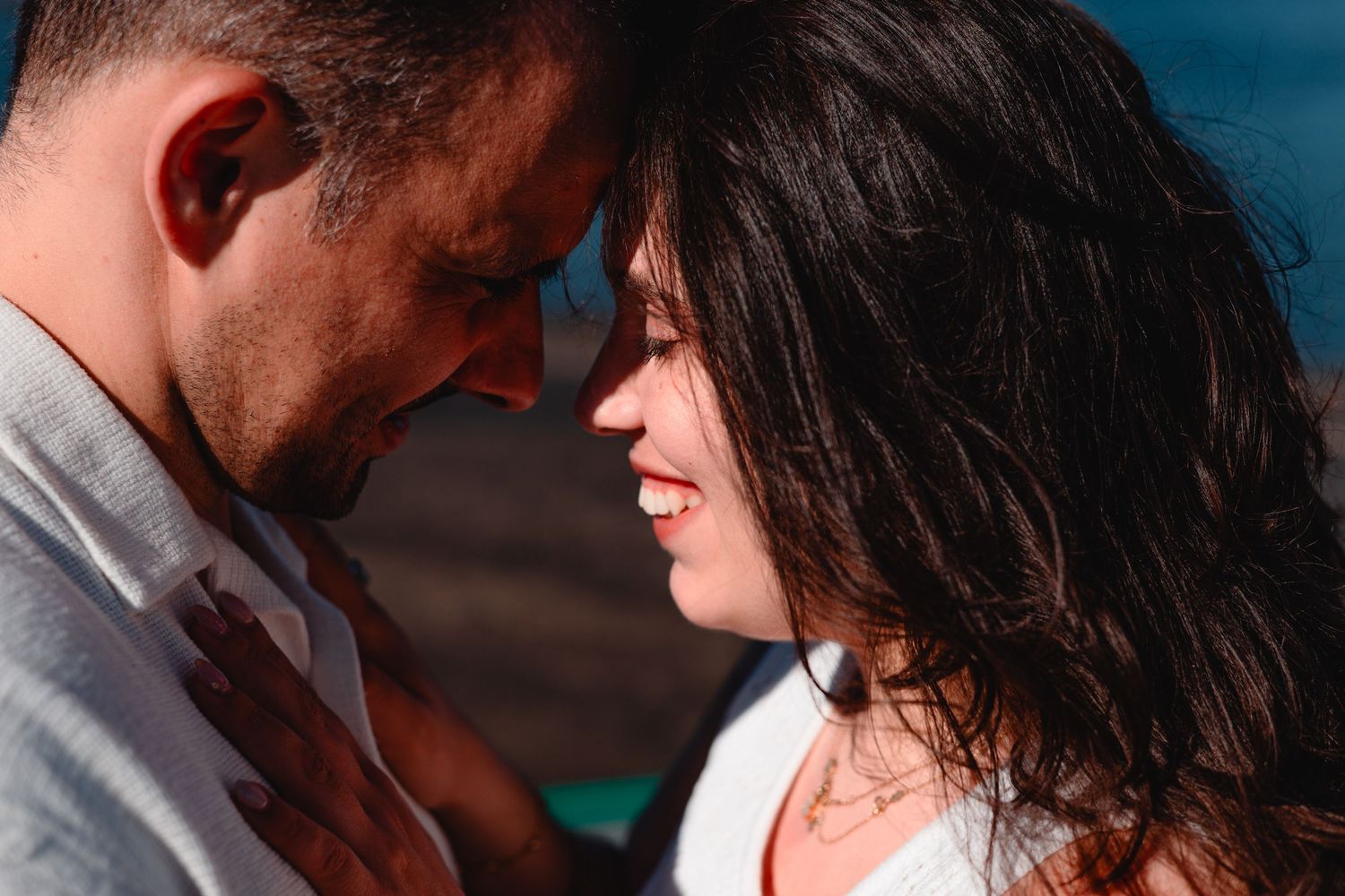 Intimate close-up portrait of couple sharing tender moment against blue background.
