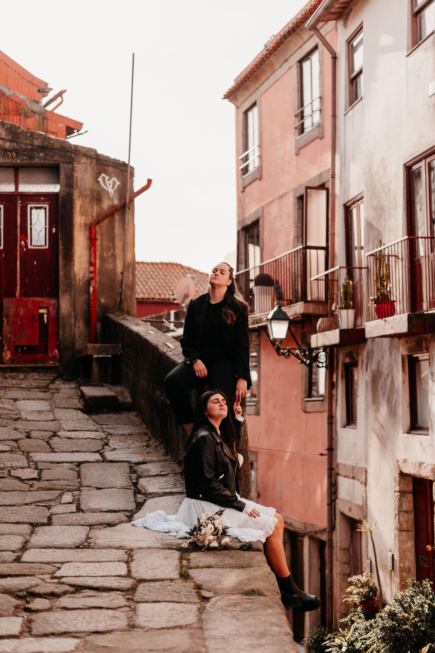 Two women posing on cobblestone steps beside colorful European buildings in Porto, Portugal.