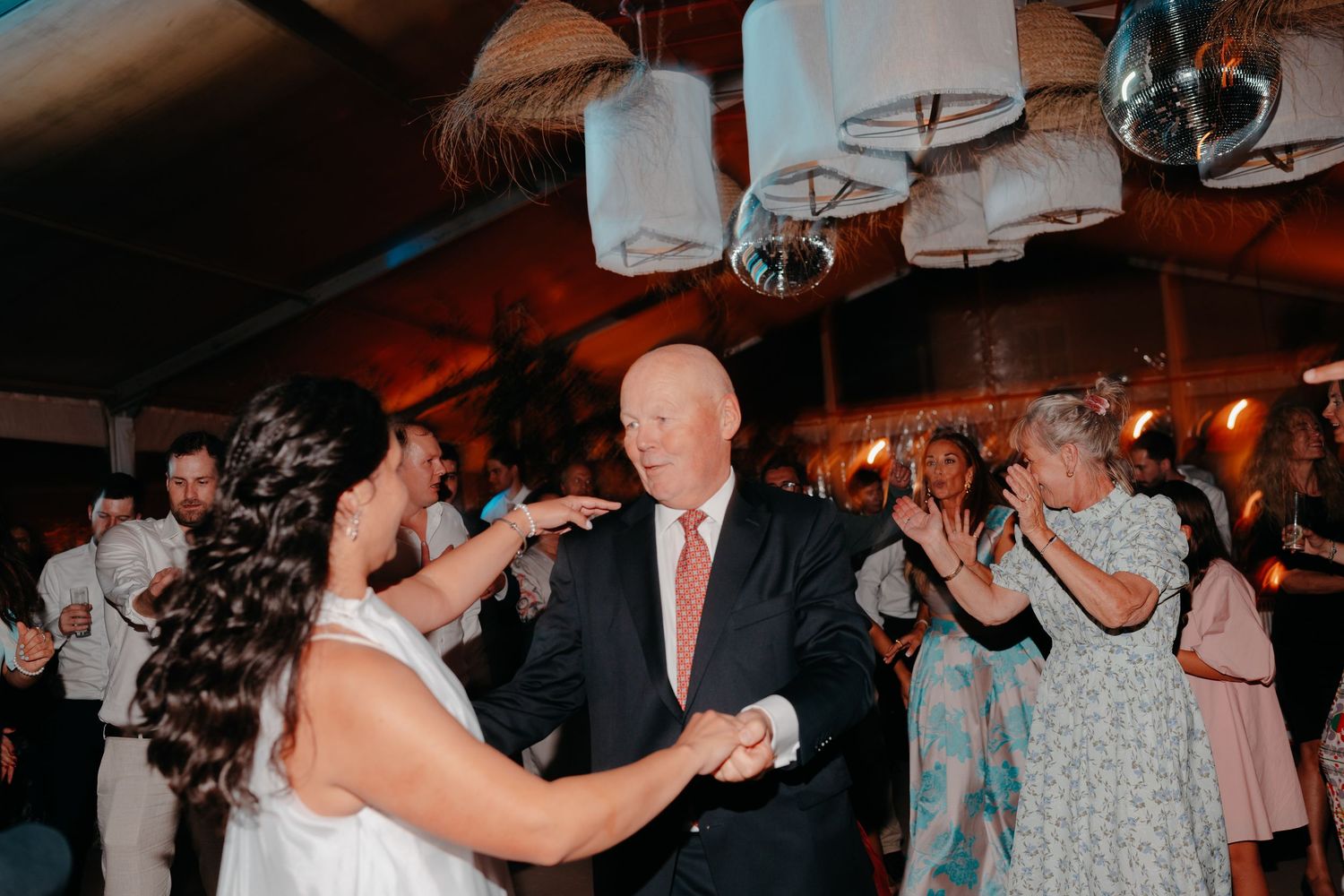 Bride and older man share a dance at a wedding reception with guests clapping in the background.