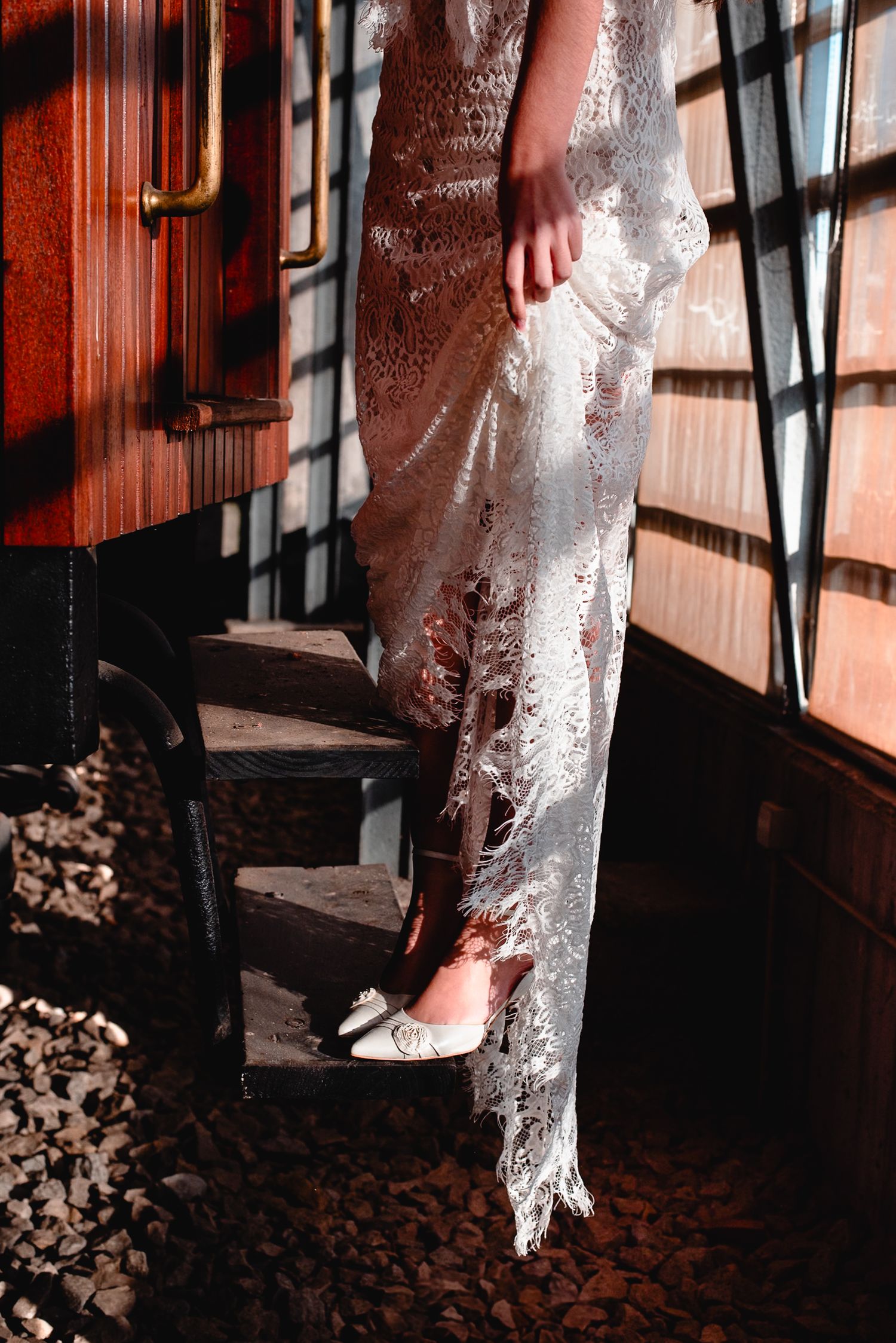 Delicate lace wedding dress details captured in dramatic lighting against rustic wooden backdrop.