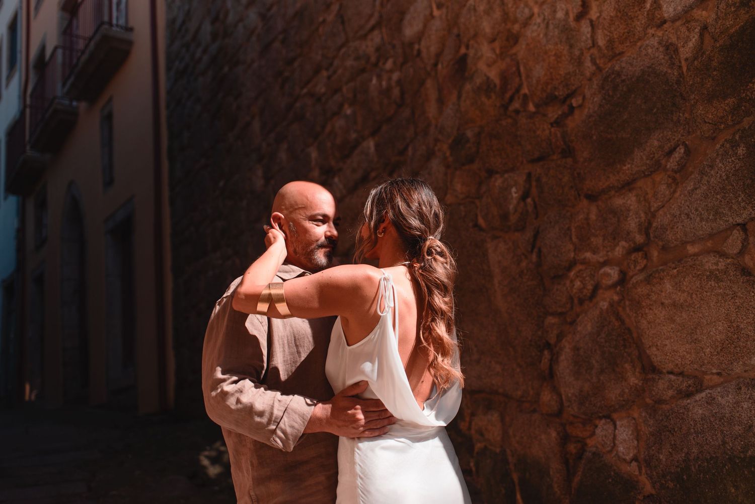 An intimate embrace photographed in a picturesque European street with rustic stone walls.