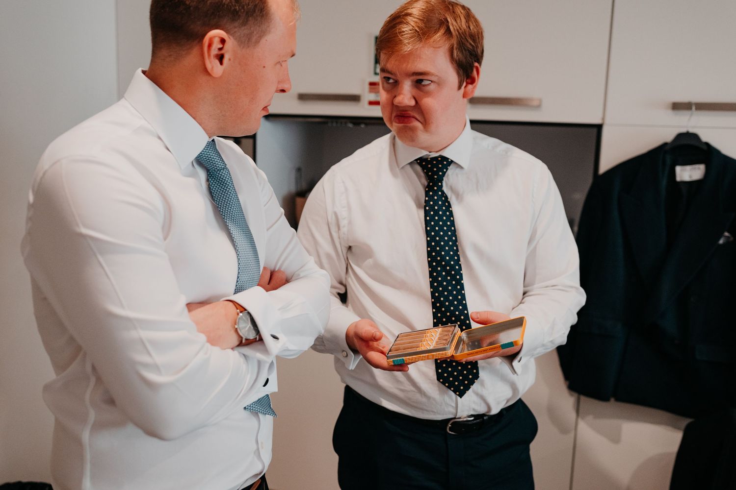 Two men in dress shirts and ties having a conversation, one holding a gift box, in a bright modern room.