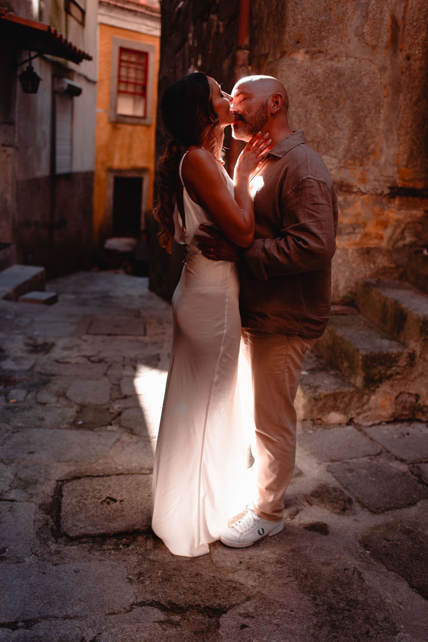 Romantic couple shares an intimate moment on cobblestone streets at sunset with dramatic lighting.