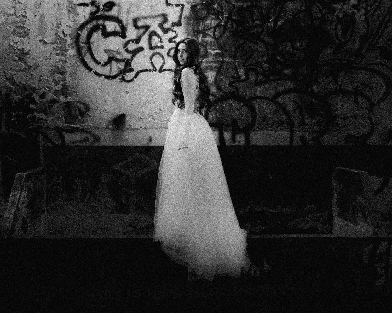 Artistic black and white photo of a wedding dress silhouette against a graffiti wall.
