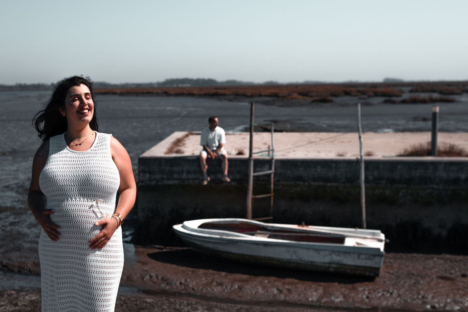 A couple poses along a scenic waterfront boardwalk at sunset with boats in the background.