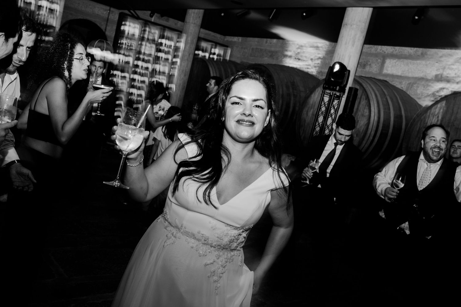 Bride dancing joyfully holding a cocktail glass at a wedding reception in black and white photo.