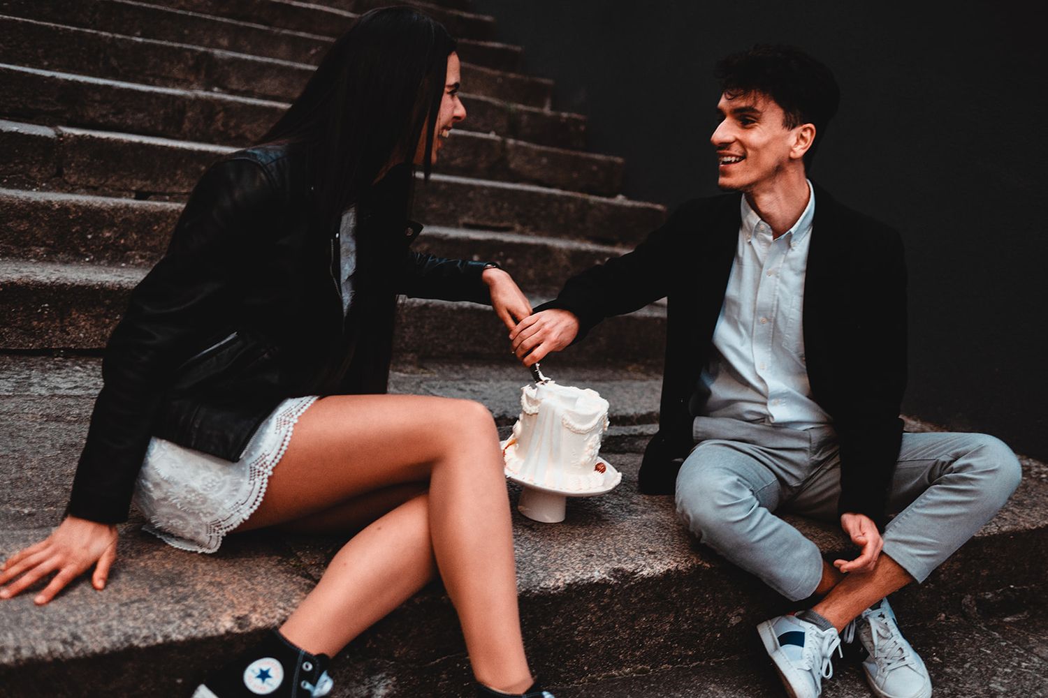 Urban fashion photography featuring legs and sneakers on dark concrete steps.