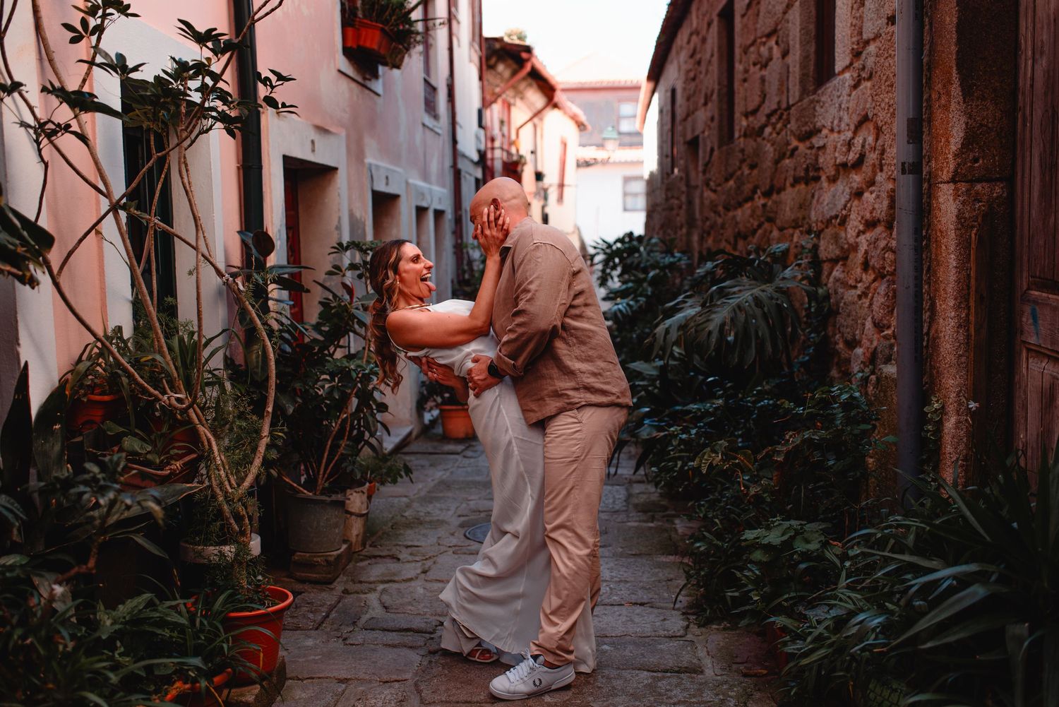 Couple dancing together in a narrow cobblestone alley with stone walls and potted plants.