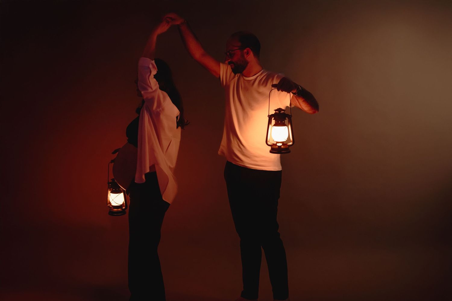 Two people holding glowing lanterns dance together in warm amber light against a dark background.
