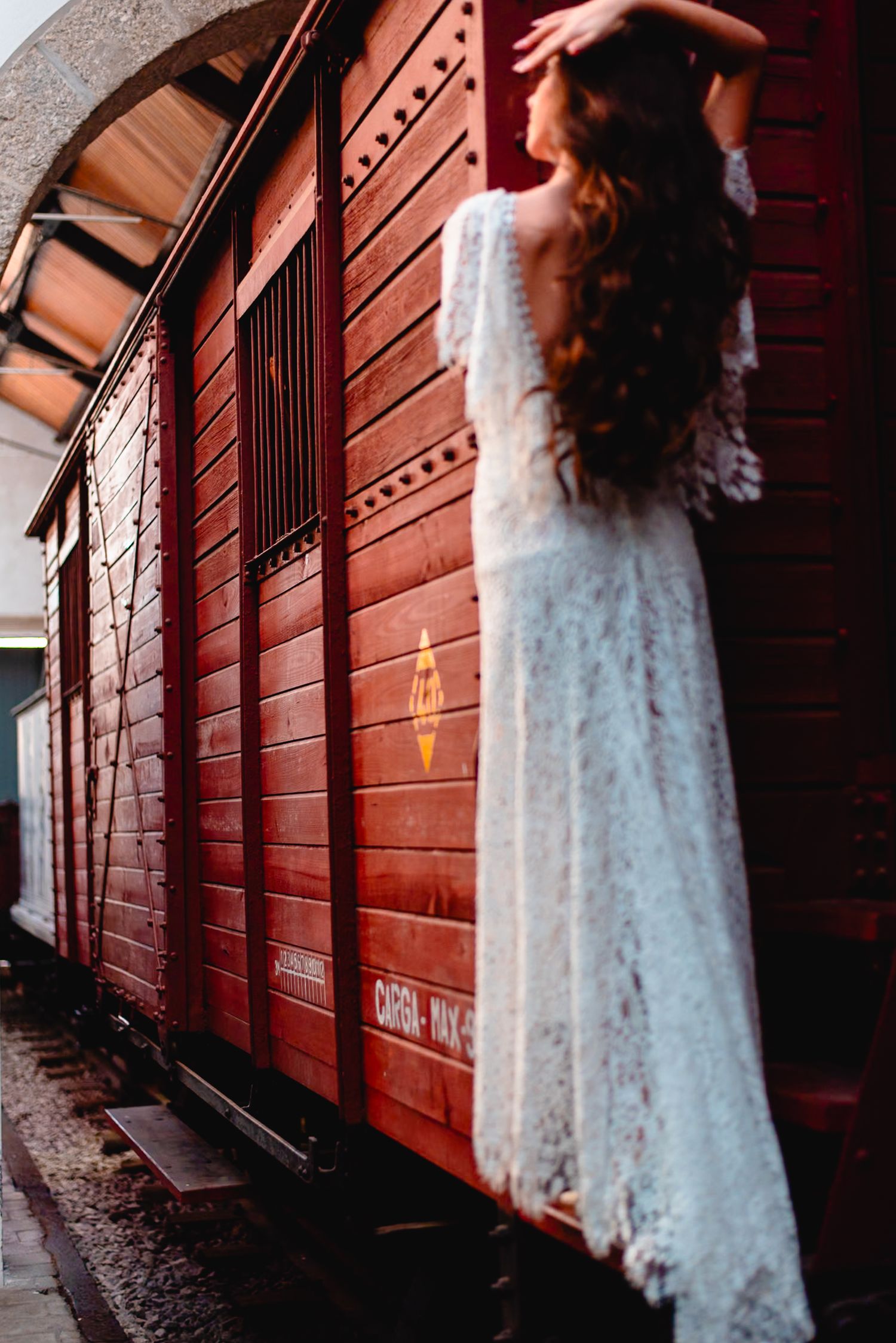 Elegant lace dress photographed in moody lighting against rustic red wooden architecture.