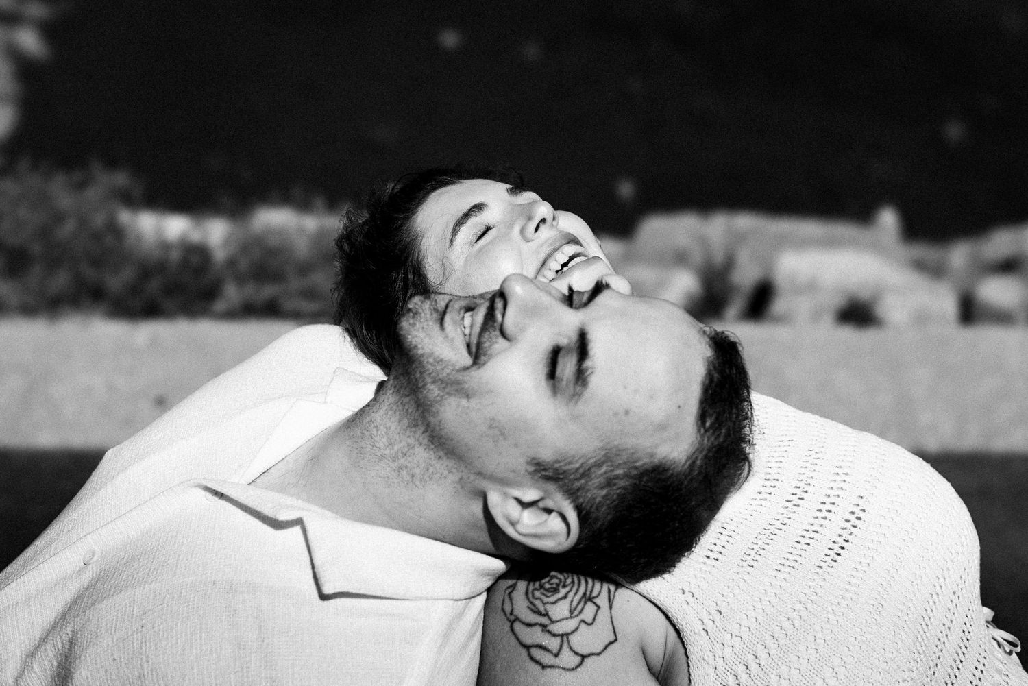 Person wearing glasses lying back and laughing joyfully in black and white photography.