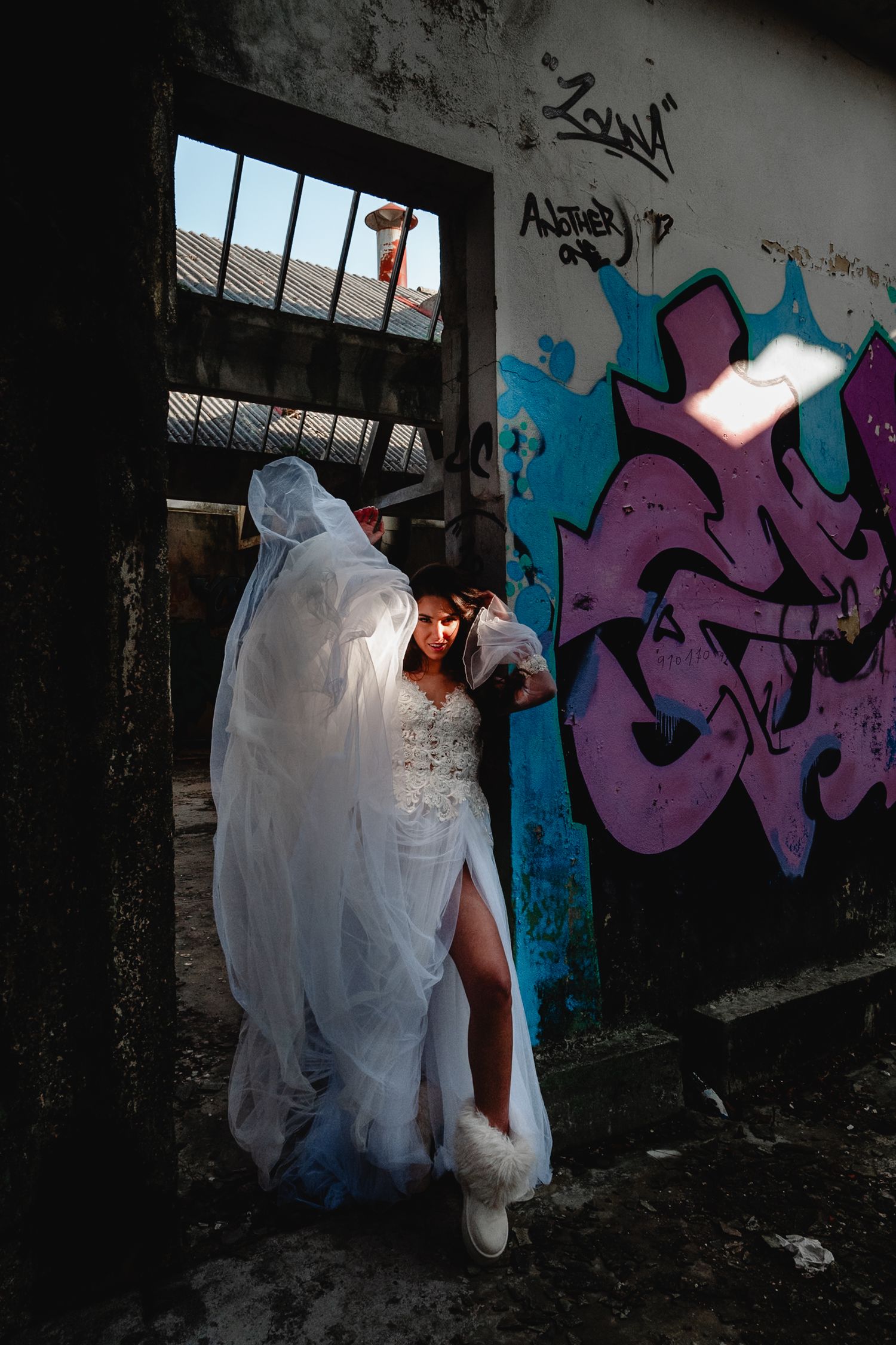 A white wedding dress photographed against a wall with vibrant blue and purple graffiti art in an urban setting.