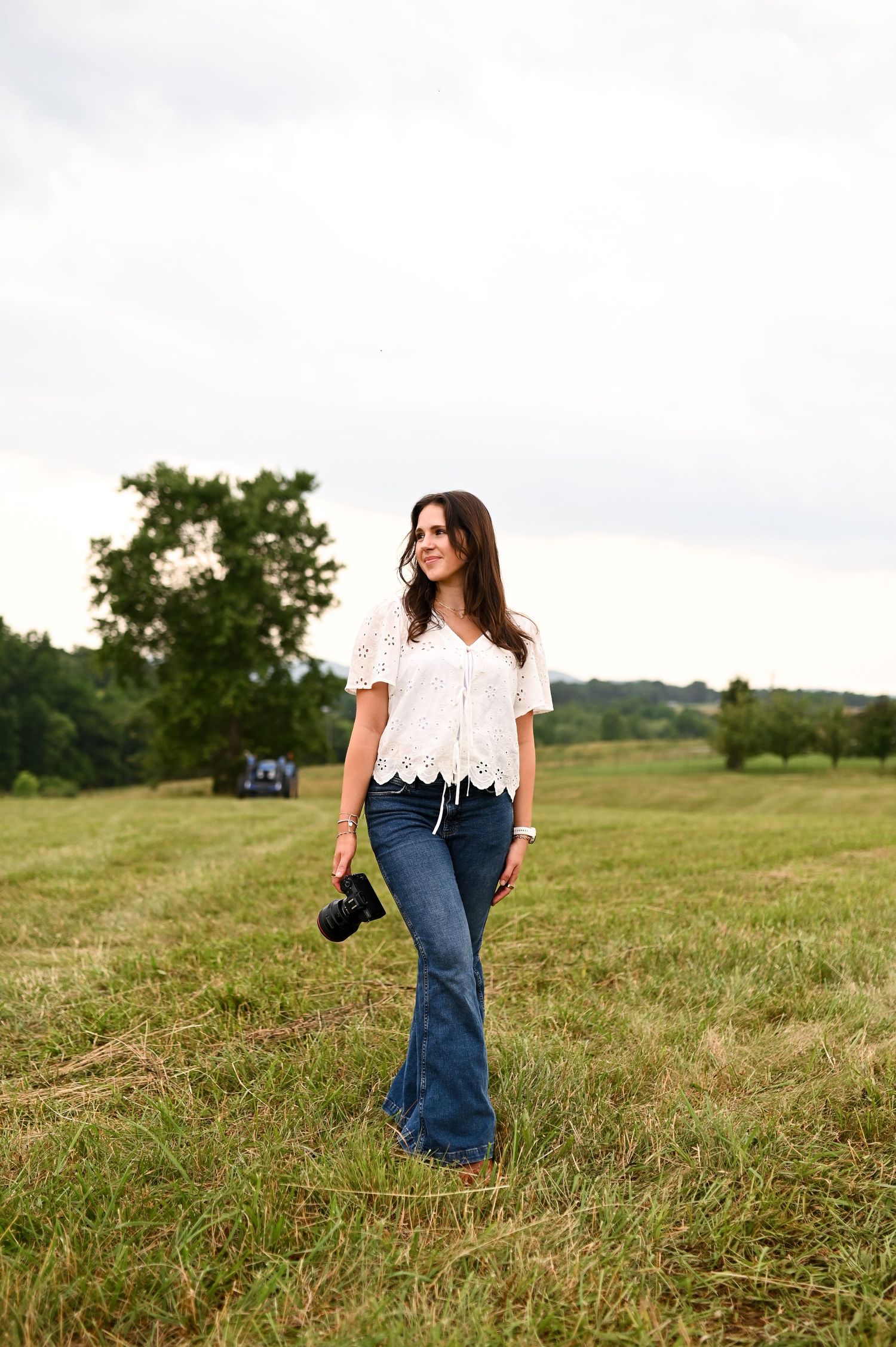 Woman walking through a field in jeans and white top during golden hour branding session in North Carolina