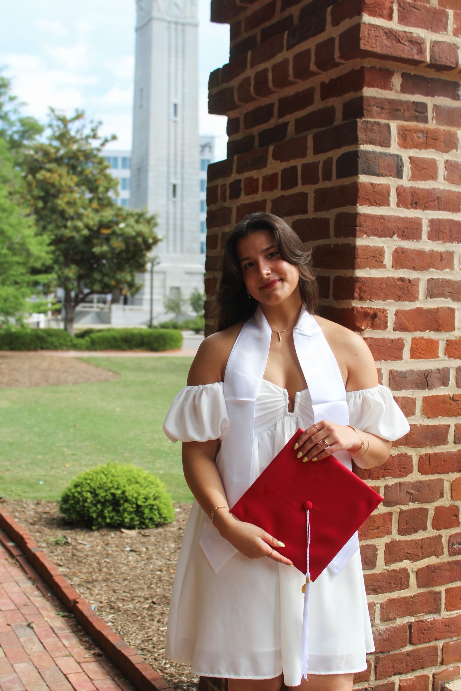 Senior girl posing in cap and gown by a brick building for NC State graduation photography session