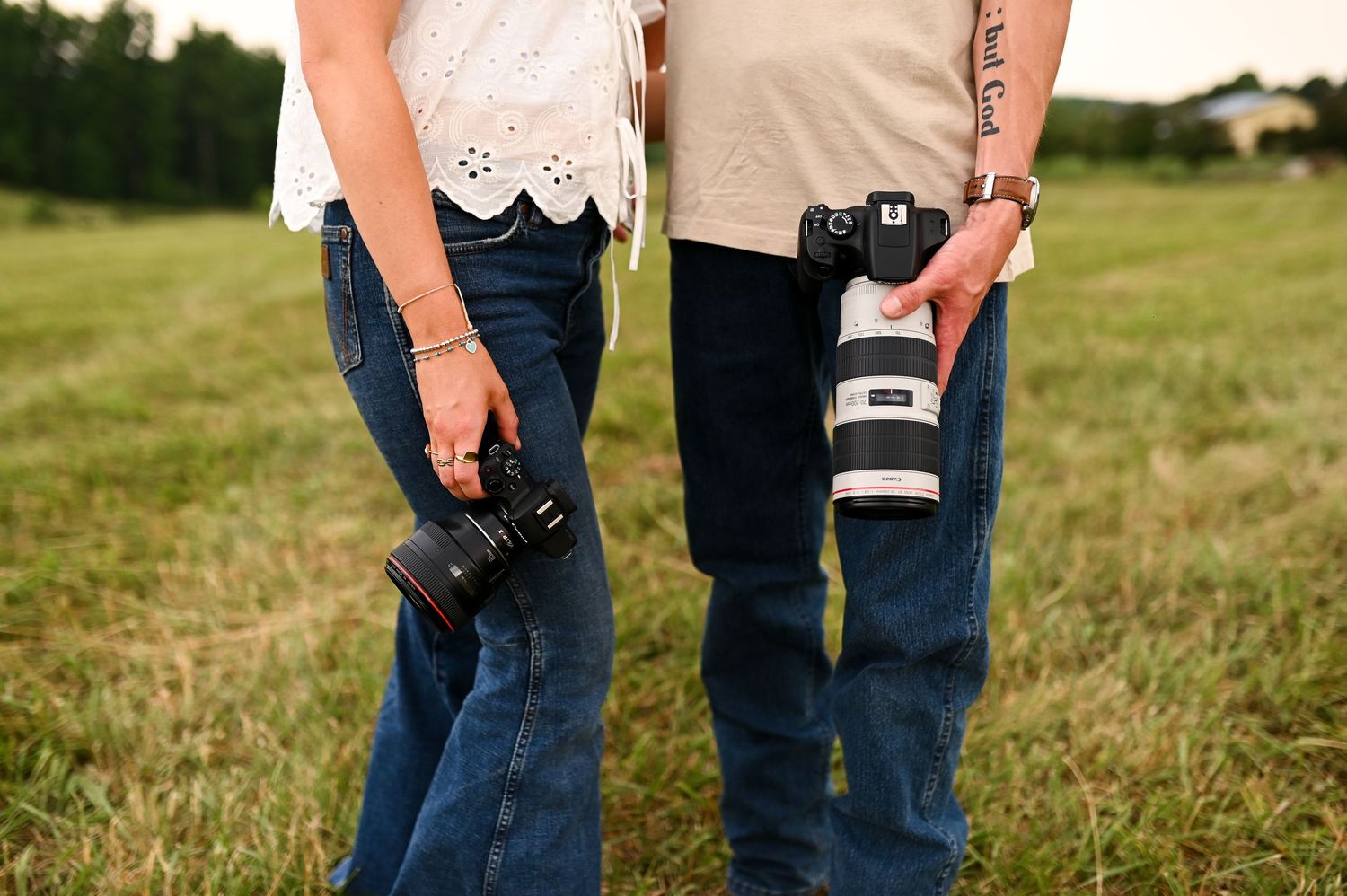Close-up of two photographers holding cameras in a grassy field for Charlotte brand photography session