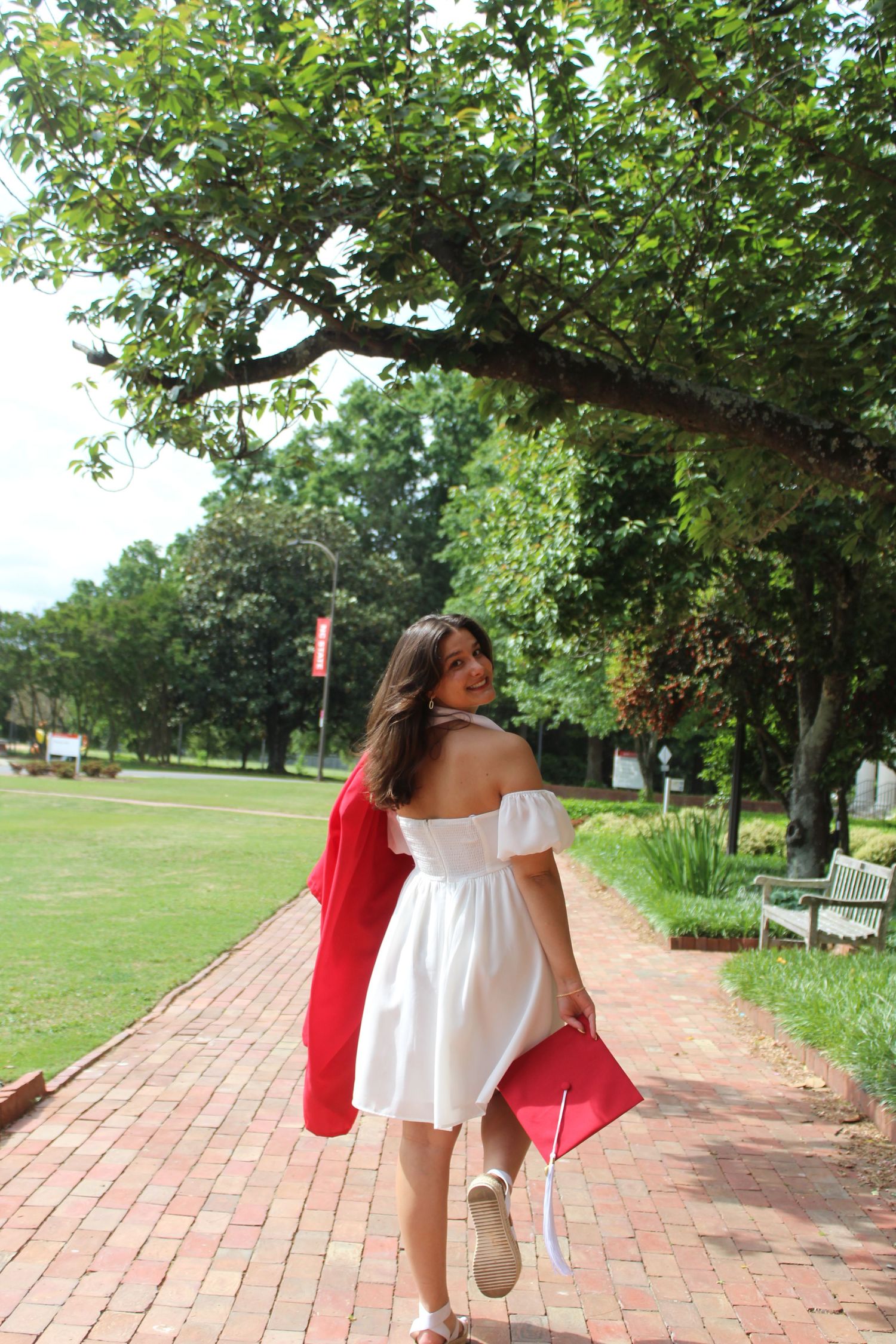 College school senior in red graduation gown walking through a historic park in Raleigh, NC