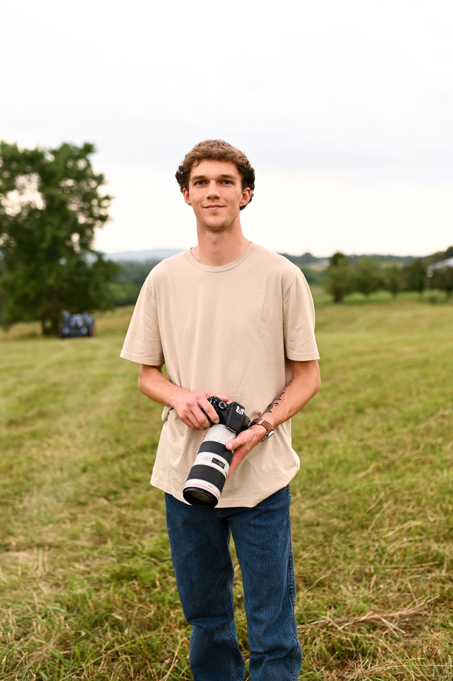 Male photographer holding a camera in a field for NC branding photography session with Still Sunday Media