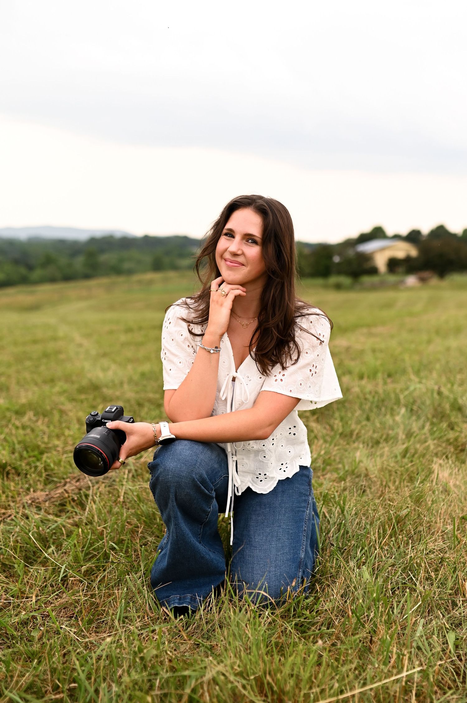 Woman kneeling in a field smiling with her camera during golden hour branding shoot for Still Sunday Media