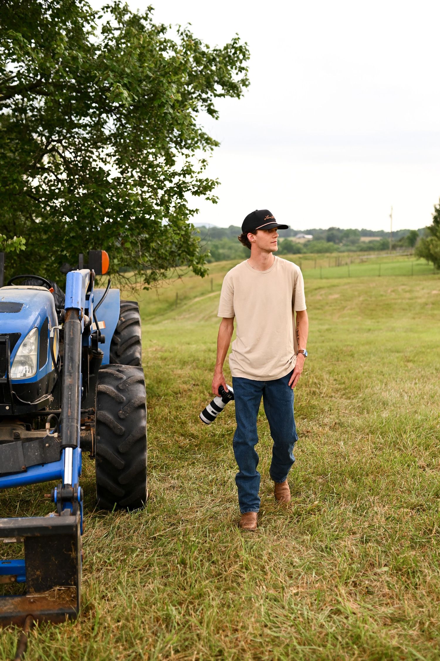 Male photographer walking toward the camera near a vintage tractor during NC lifestyle photo session