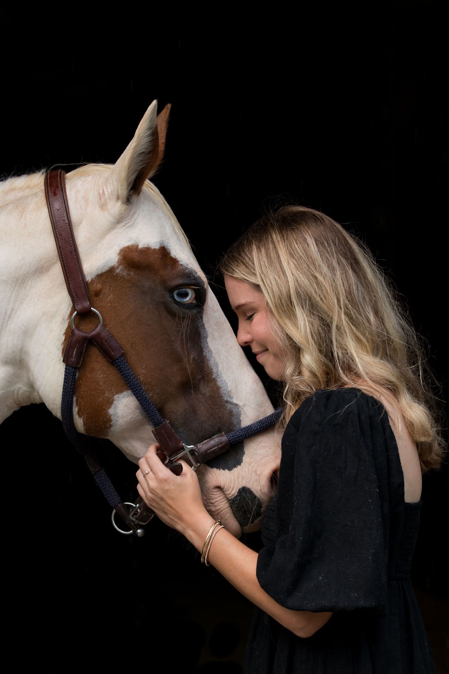 Woman in black dress kissing her white horse in a black background equine portrait session