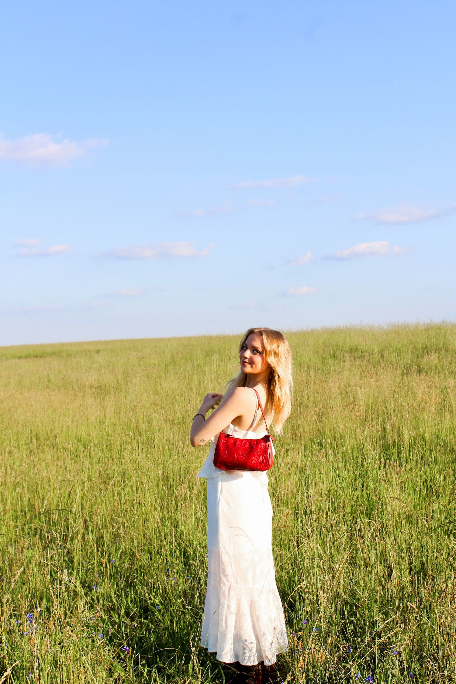 Senior girl in white dress and red cap posing in a wide field for graduation photography in Charlotte, NC