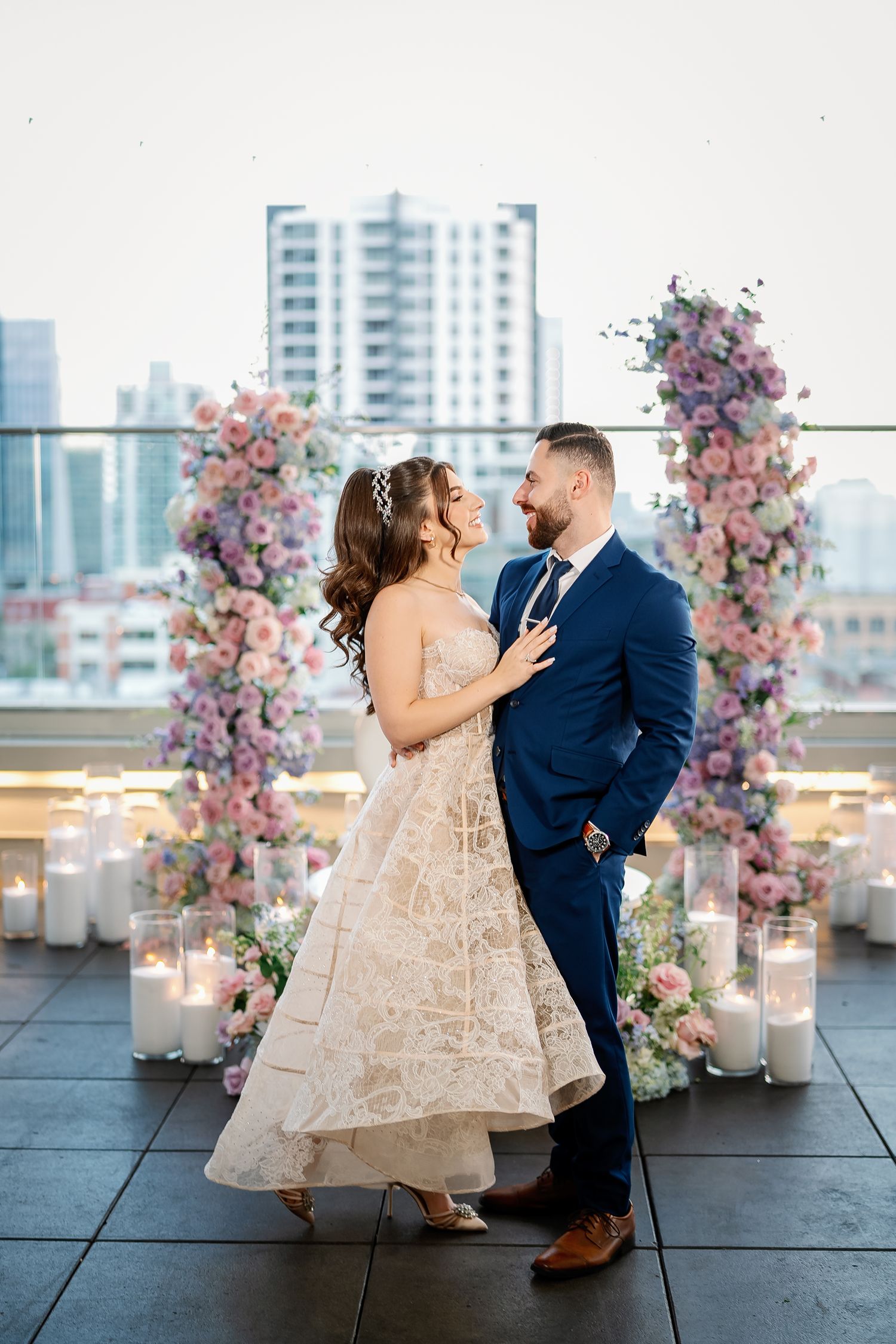 Couple dances on rooftop venue decorated with pink floral arrangements and city skyline backdrop.