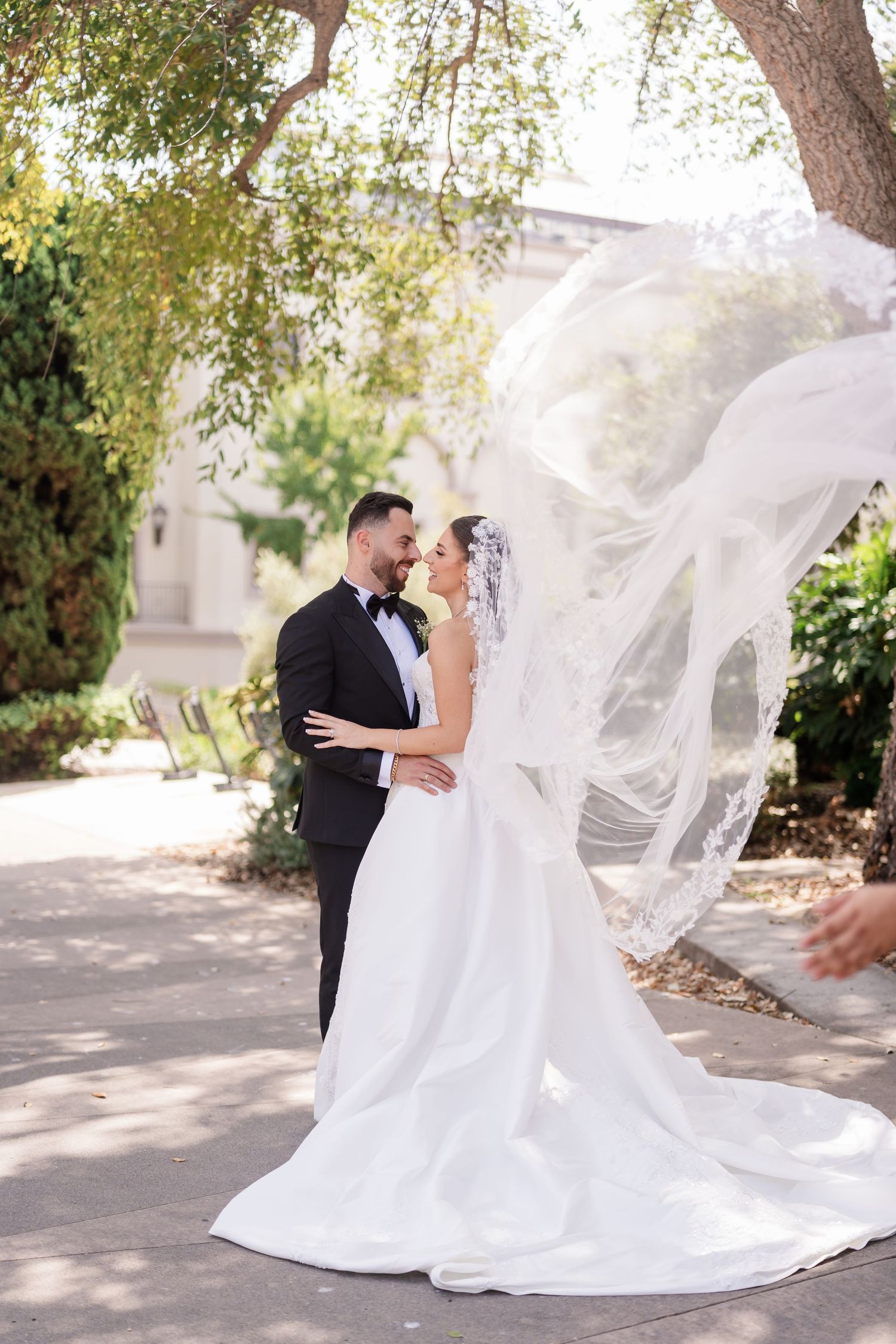 A dramatic wedding photo with a flowing veil catching the breeze in a garden setting.