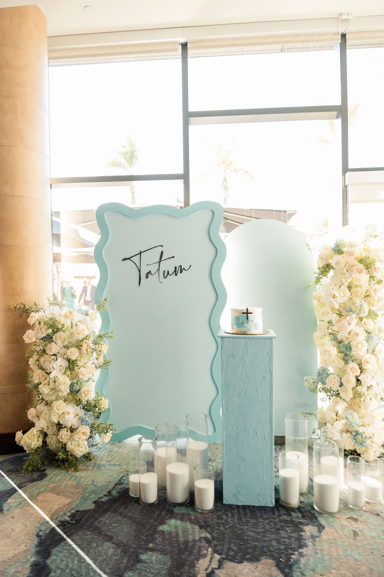 Elegant mint green wedding decor setup with scalloped backdrop, white floral arrangements and glowing candles by window.
