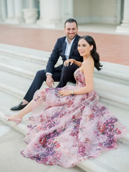 Couple relaxing on white stone steps in formal attire with flowing pink floral dress.