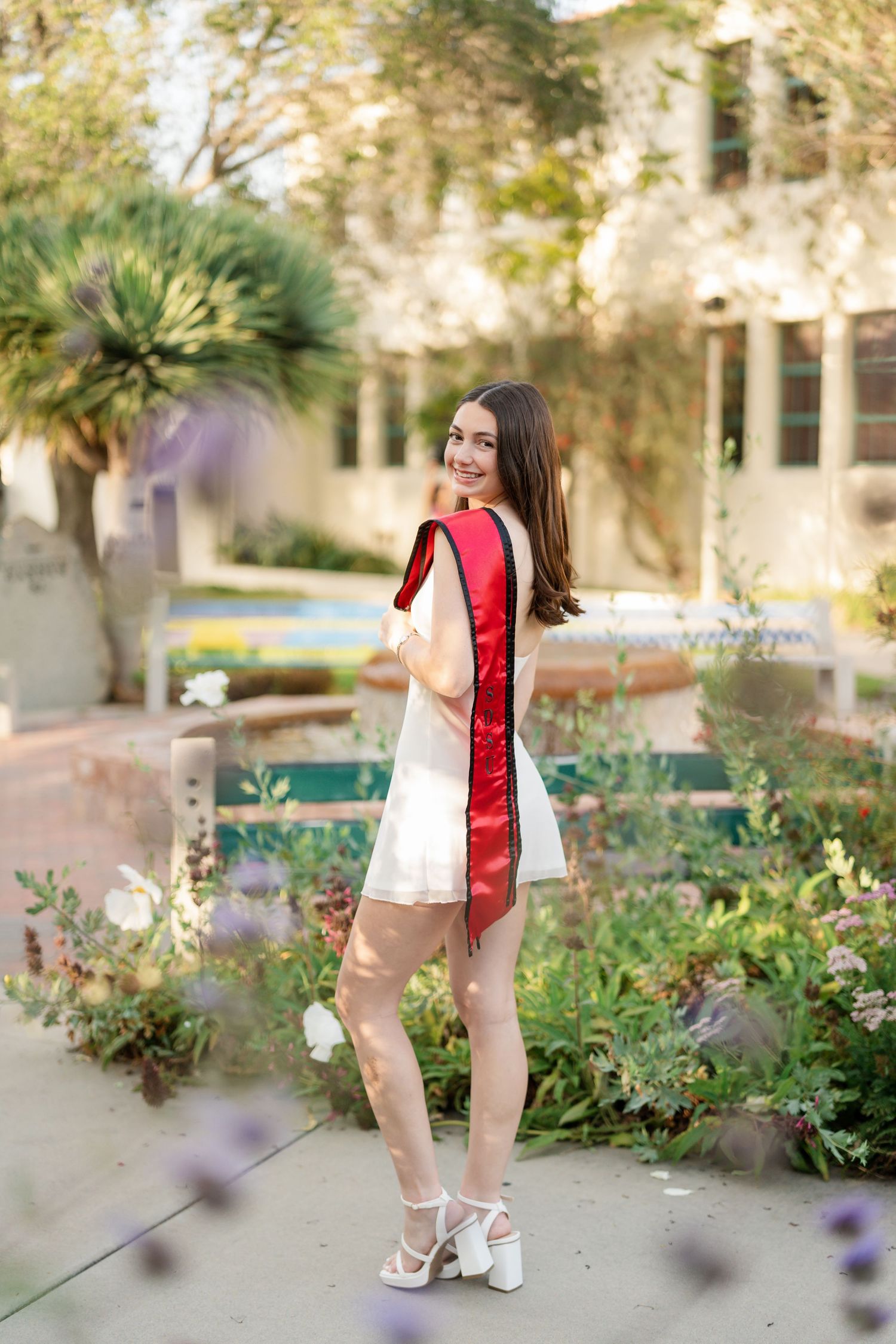 Graduation photos captured in a garden setting with blooming flowers and Mediterranean architecture.