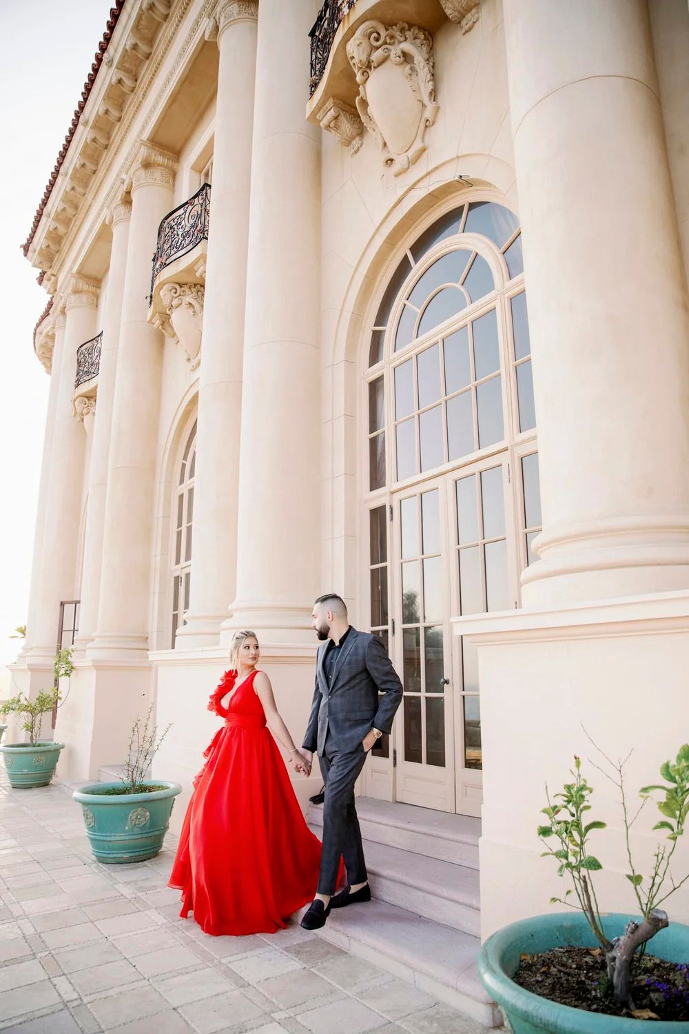 A couple stands outside a neoclassical building with grand columns and arched windows.