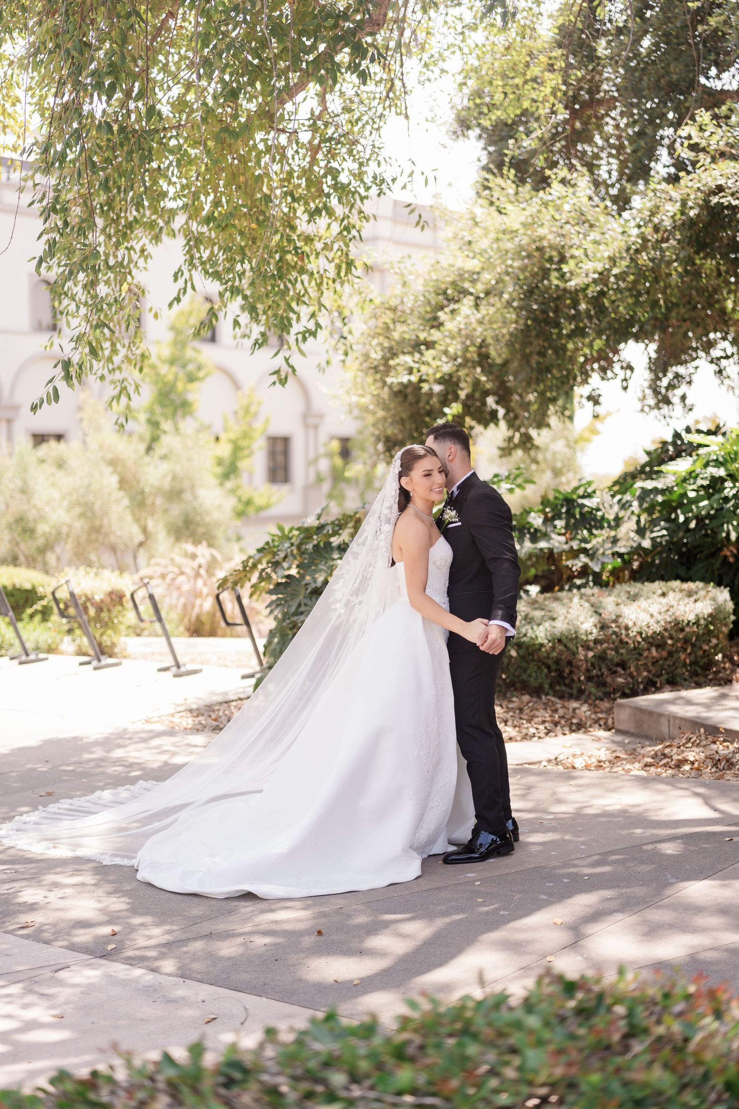A sunlit garden wedding portrait featuring a classic white gown with a trailing veil.