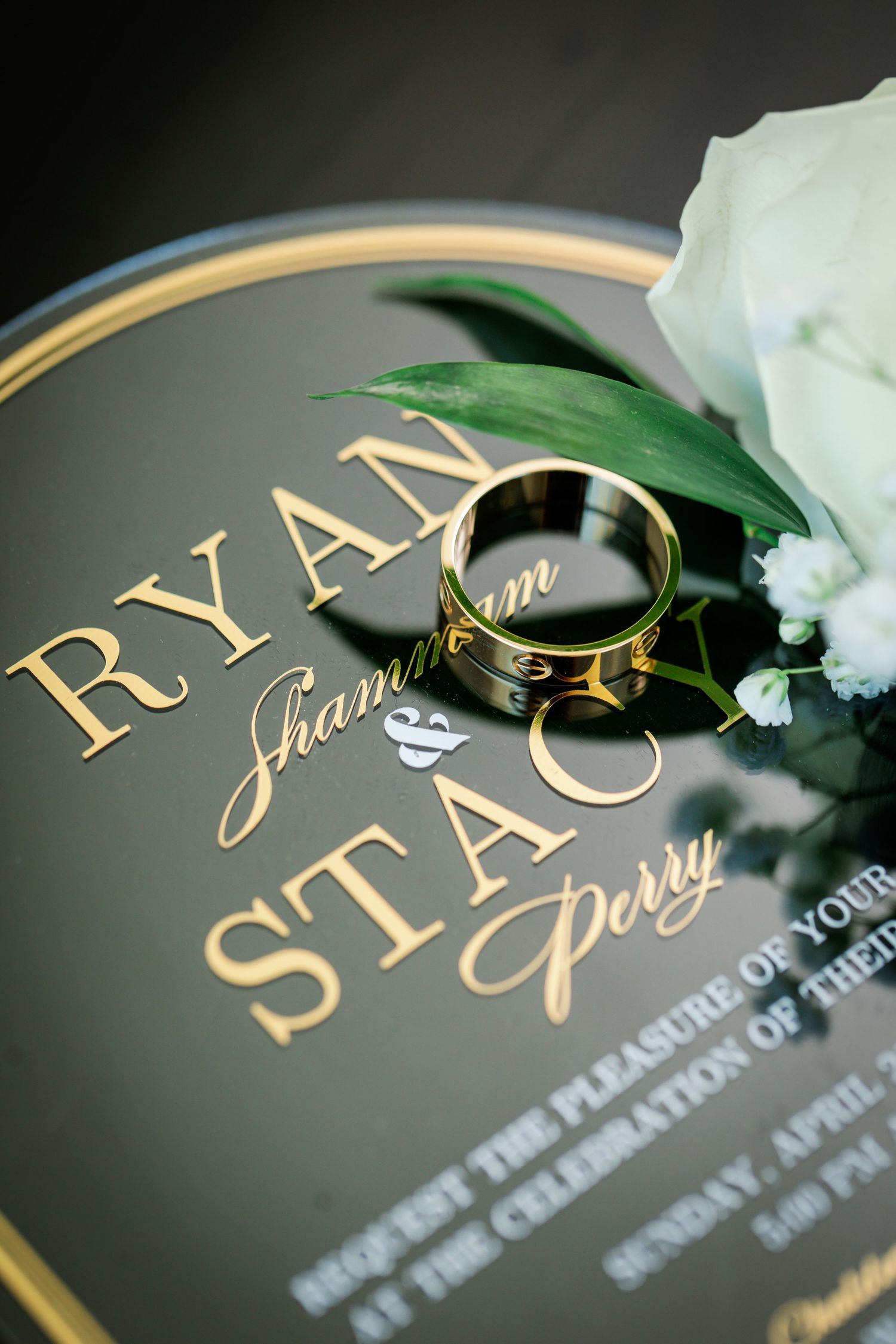 Elegant wedding invitation with gold lettering and white floral details on dark background.