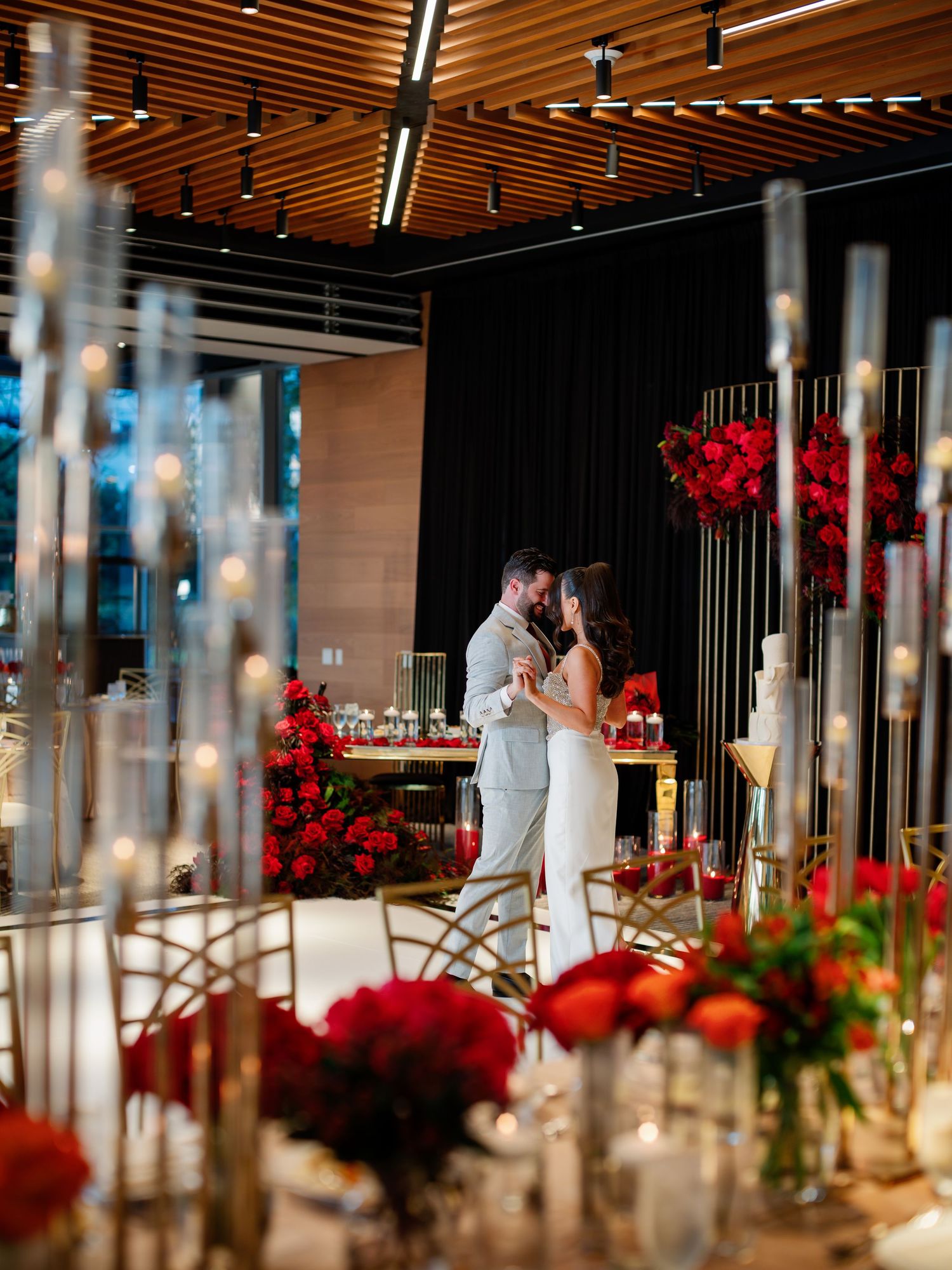 An elegant reception table setting with red floral arrangements and glowing candlelight.