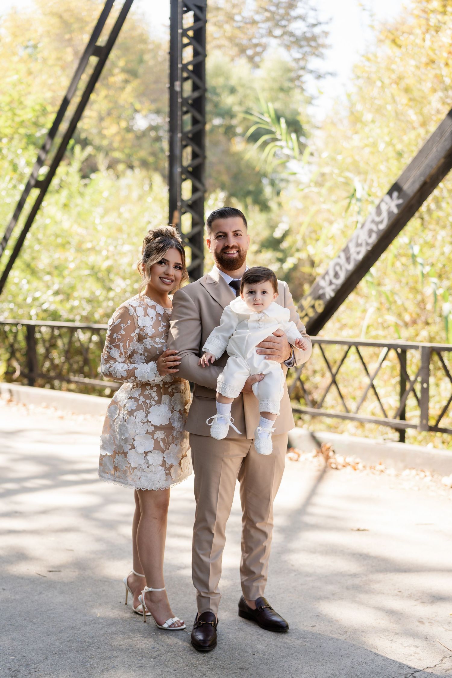A family in coordinated beige and white outfits poses together outdoors on a sunny autumn day.