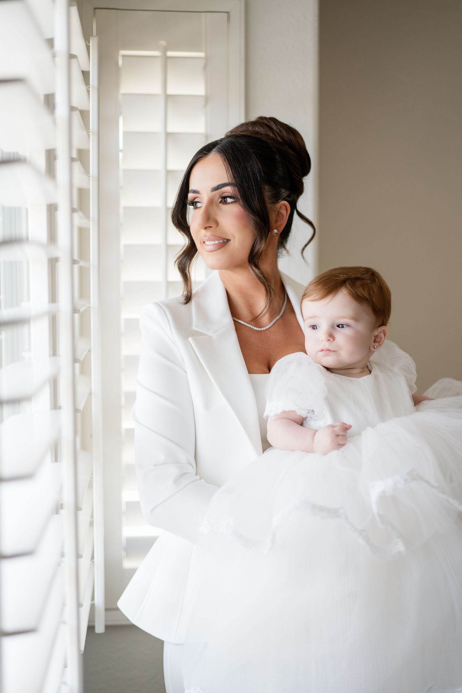A series of tender moments between a mother and baby in white clothing by a window with natural light streaming in.