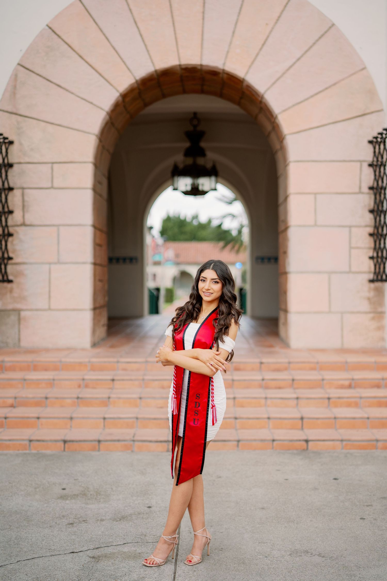 A series of graduation photos taken under arched walkways with red academic regalia.