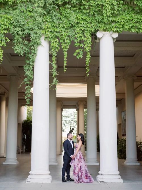 Elegant couple photographed between white columns with green foliage overhead.
