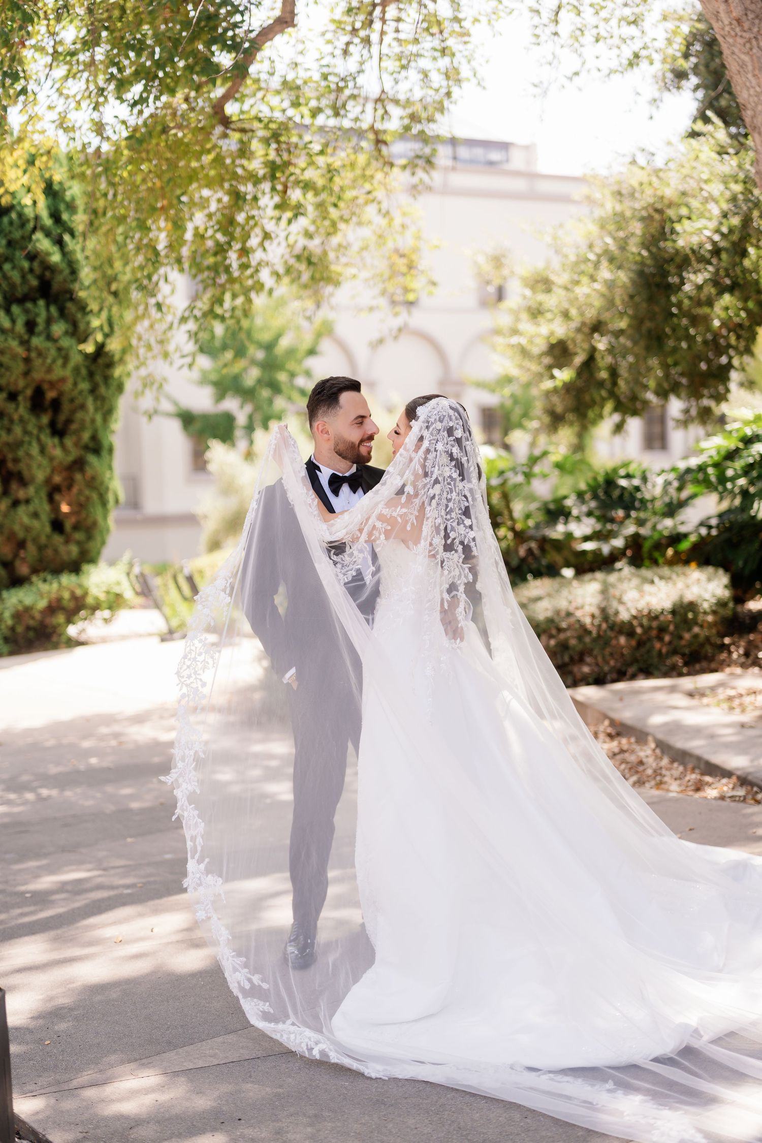 An artistic wedding portrait with dramatic lighting and a flowing lace veil in a garden setting.