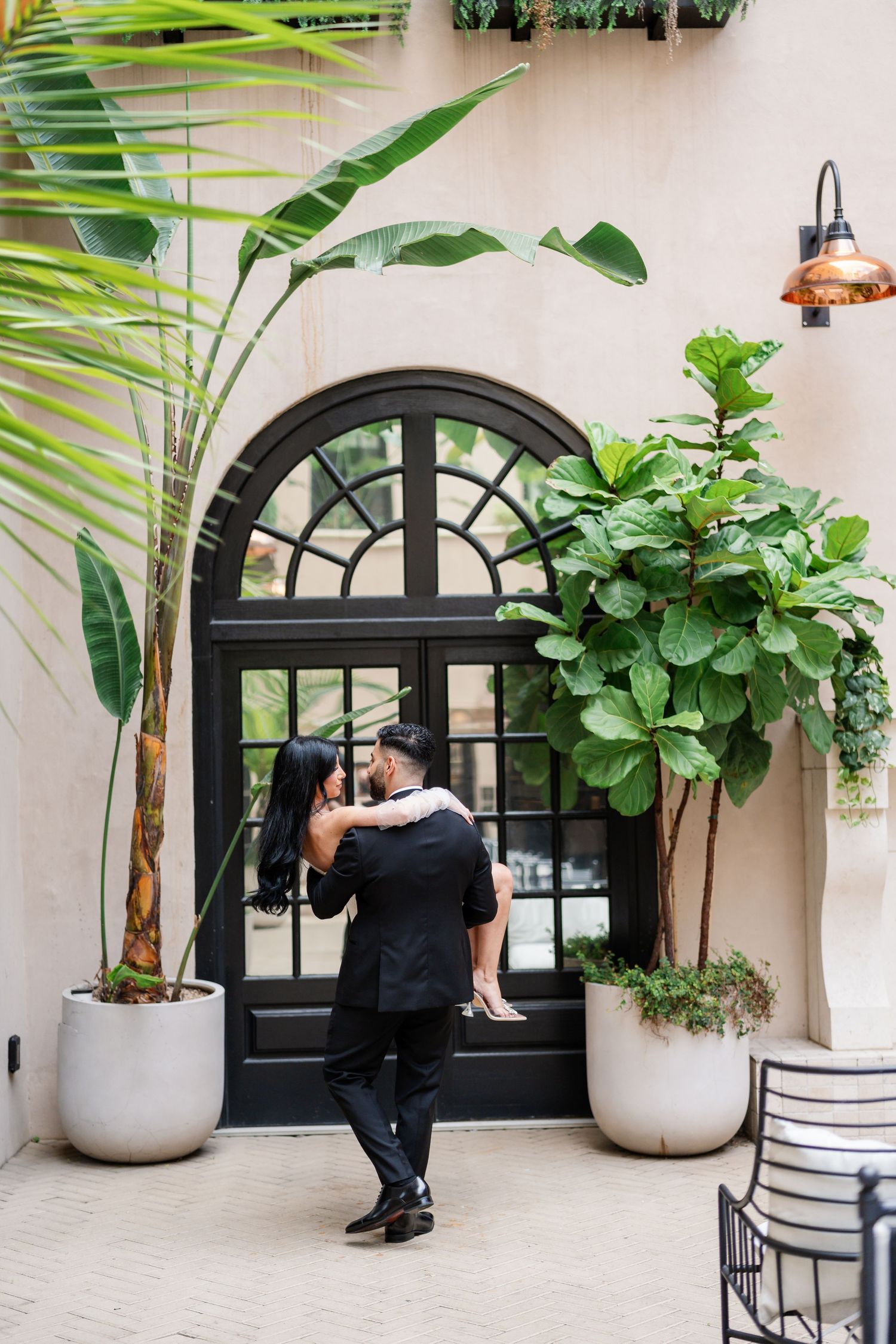 Romantic photoshoot in elegant courtyard with tropical plants and arched windows.