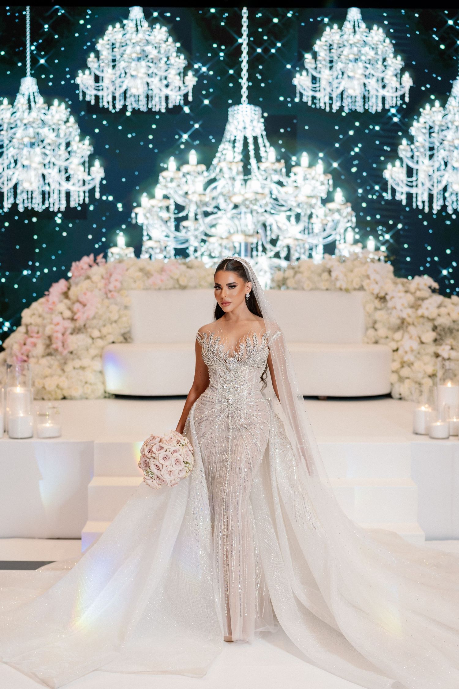 Luxurious wedding reception setup with crystal chandeliers and white floral arrangements.