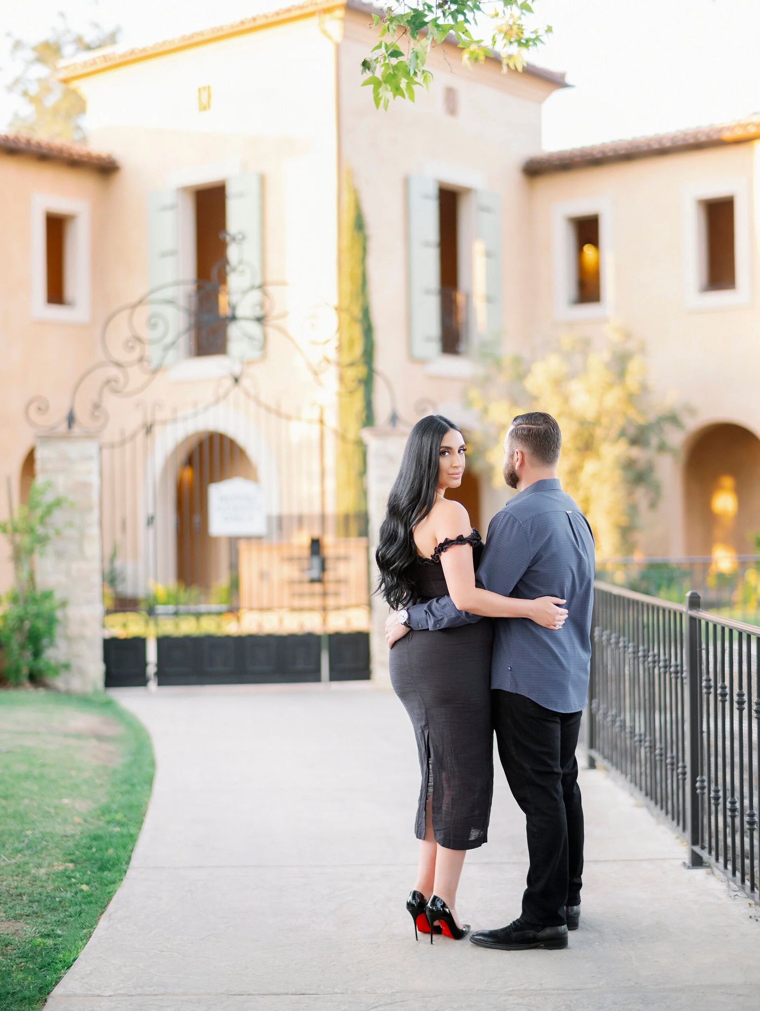 A couple shares a romantic moment along a Mediterranean-style building's walkway at sunset.