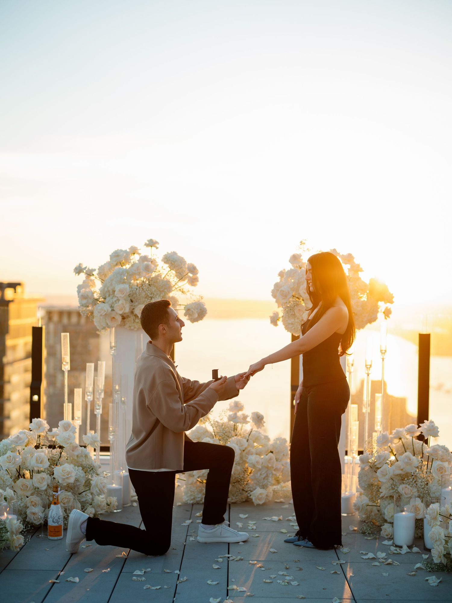 A romantic proposal scene at sunset with white floral arrangements and pillars.