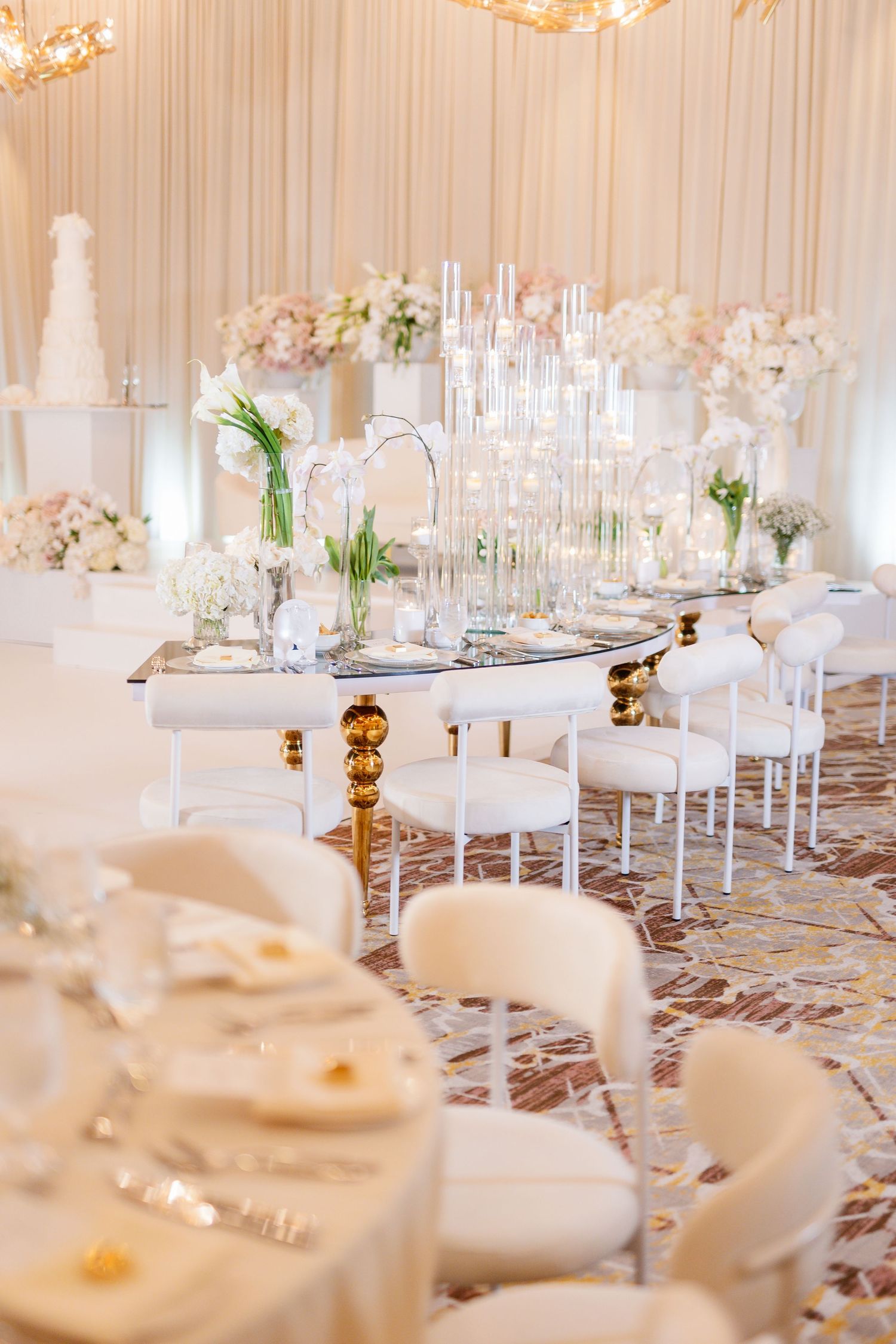 White and gold wedding reception tables set with elegant glassware and floral arrangements.