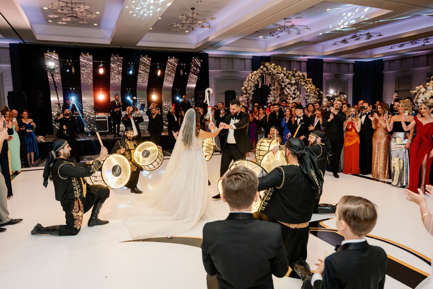 Wedding reception ballroom with guests gathered around dance floor under crystal chandeliers.
