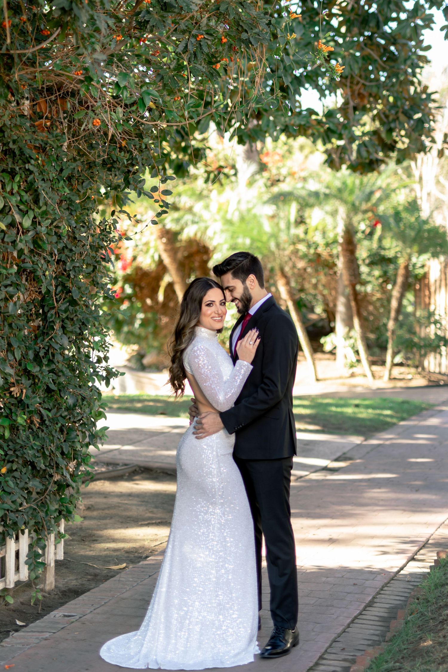 Couple shares intimate moment on tree-lined pathway during wedding photoshoot.