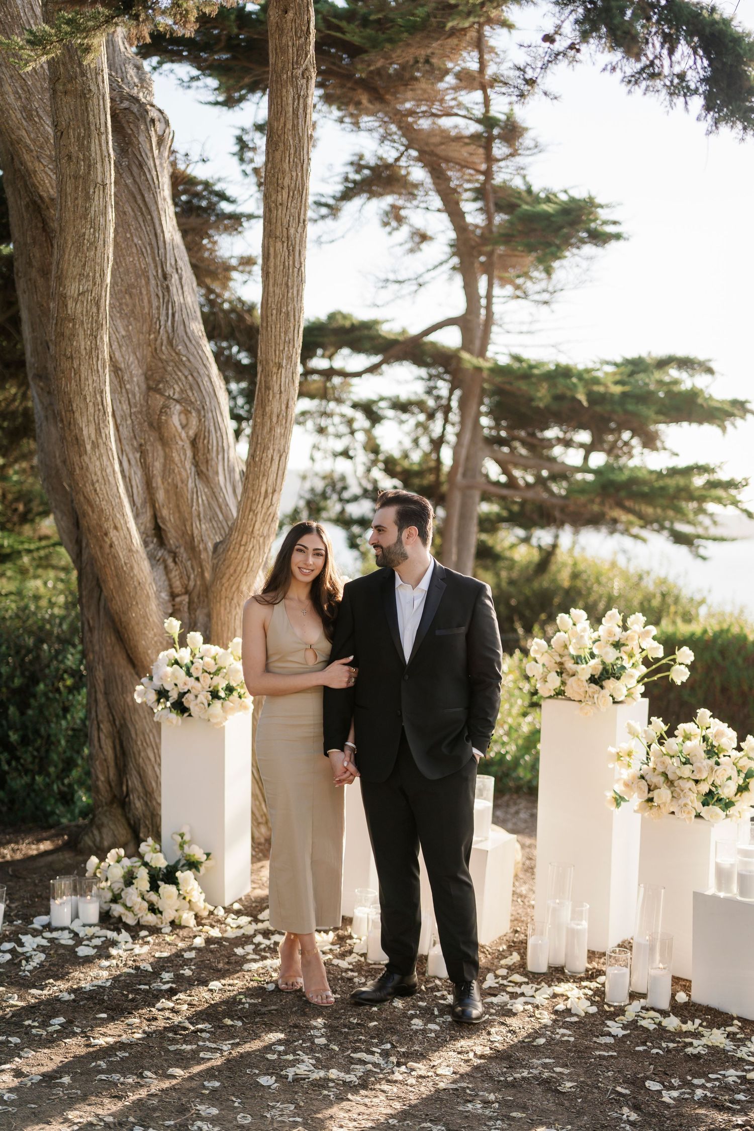 A couple poses together along a path decorated with white floral arrangements.