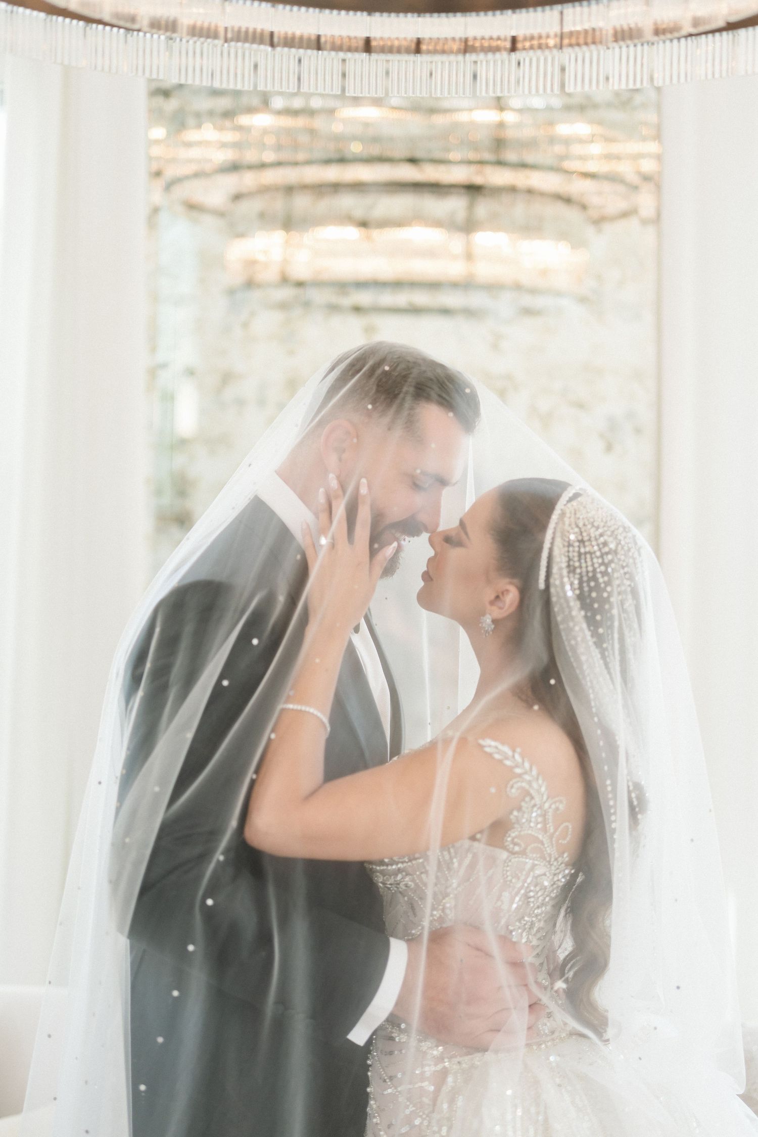 Romantic wedding portrait through a sheer veil in a light-filled space.