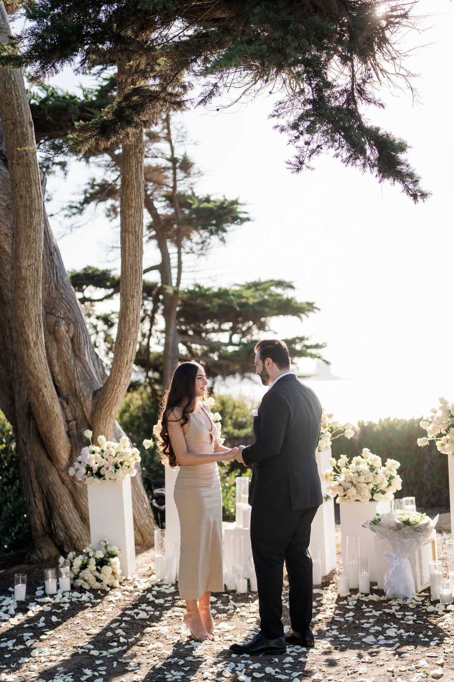White floral arrangements line a scenic outdoor path between tall trees.